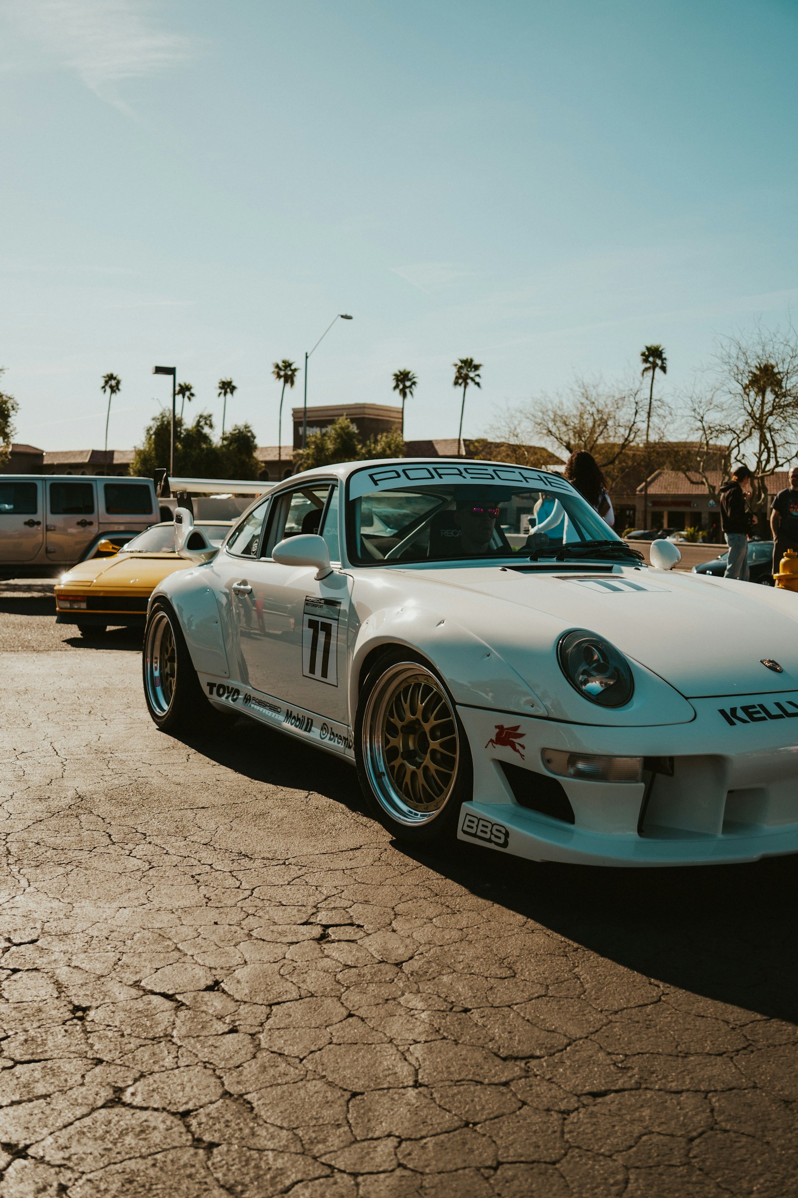 A light-colored vehicle photographed on a sunny day in a busy parking area